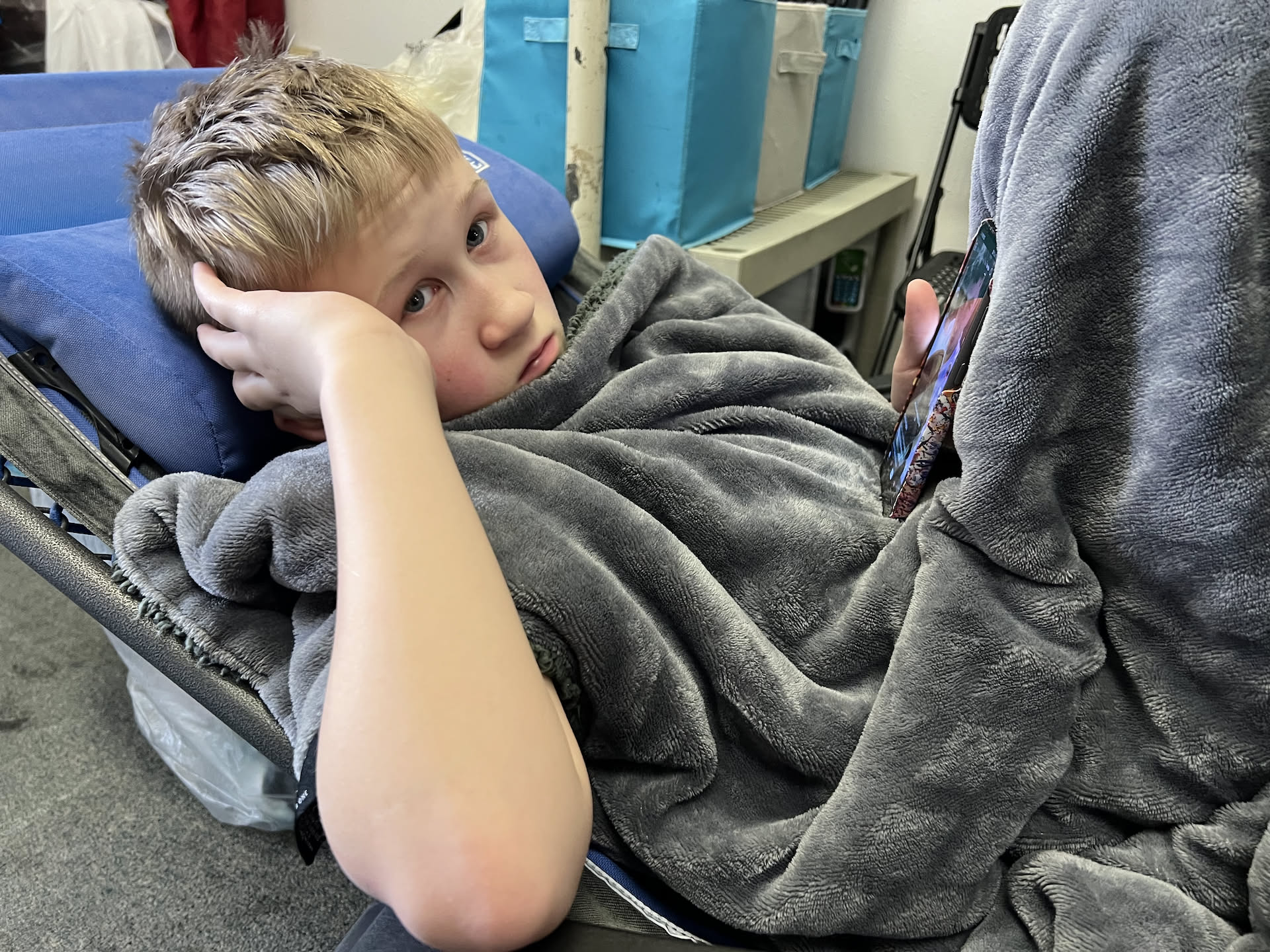 Ethan bored scrolling cuddled up in a blanket waiting for our time at the laundromat to be over.